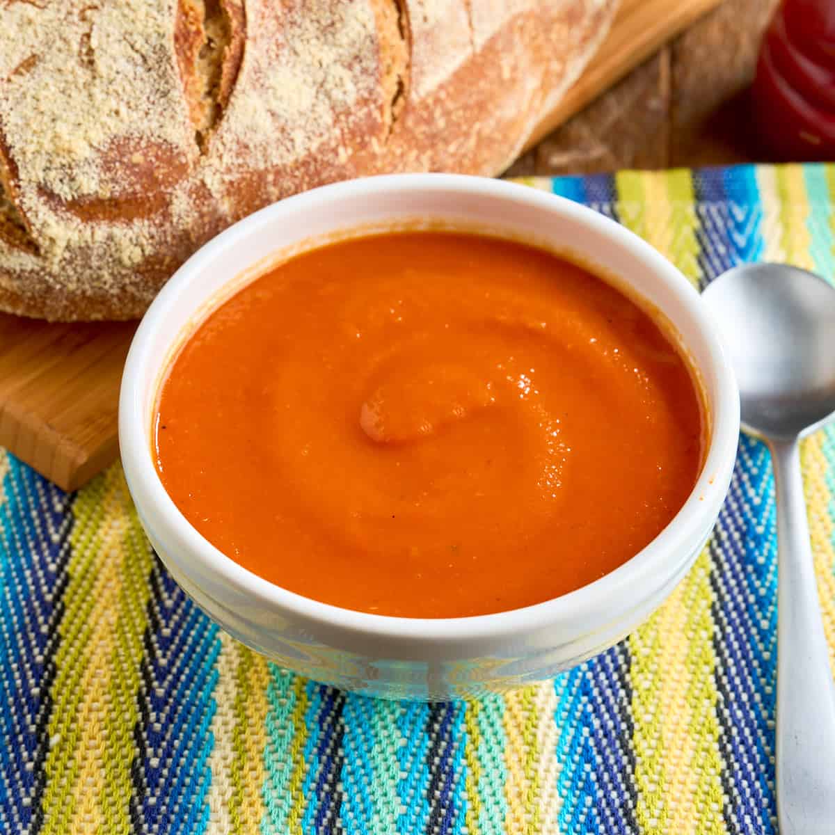 A bowl of Instant Pot Tomato Soup with a spoon and a loaf of bread