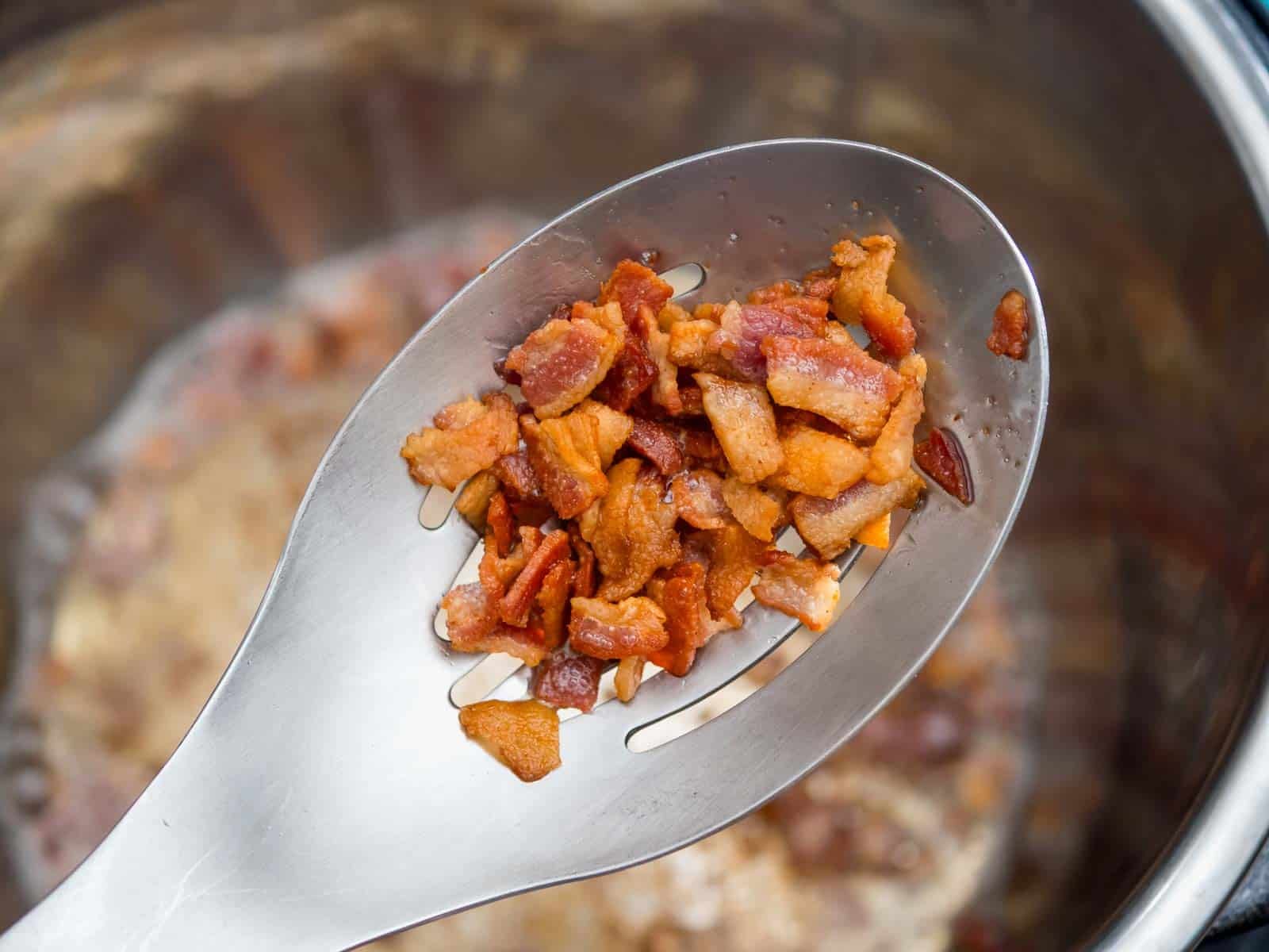 A slotted spoon full of crisped bacon