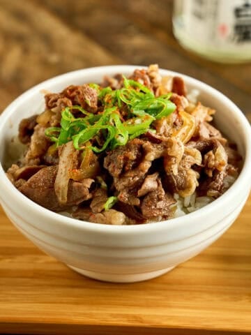 A bowl of gyudon topped with sliced green onions and shichimi togarashi