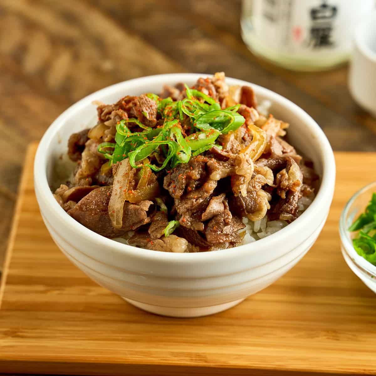 A bowl of gyudon topped with sliced green onions and shichimi togarashi