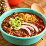 A bowl of Instant Pot Elk Chili topped with cheese, green onions, and pickled jalapenos