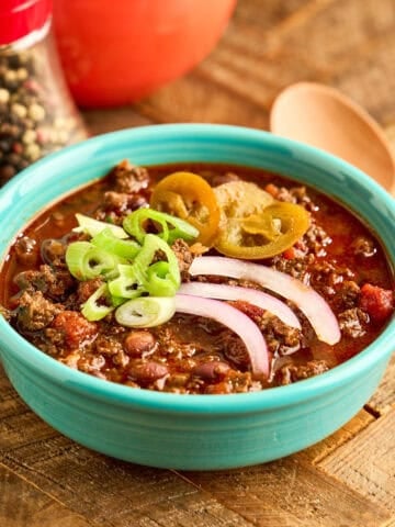 A bowl of Instant Pot Elk Chili topped with cheese, green onions, and pickled jalapenos