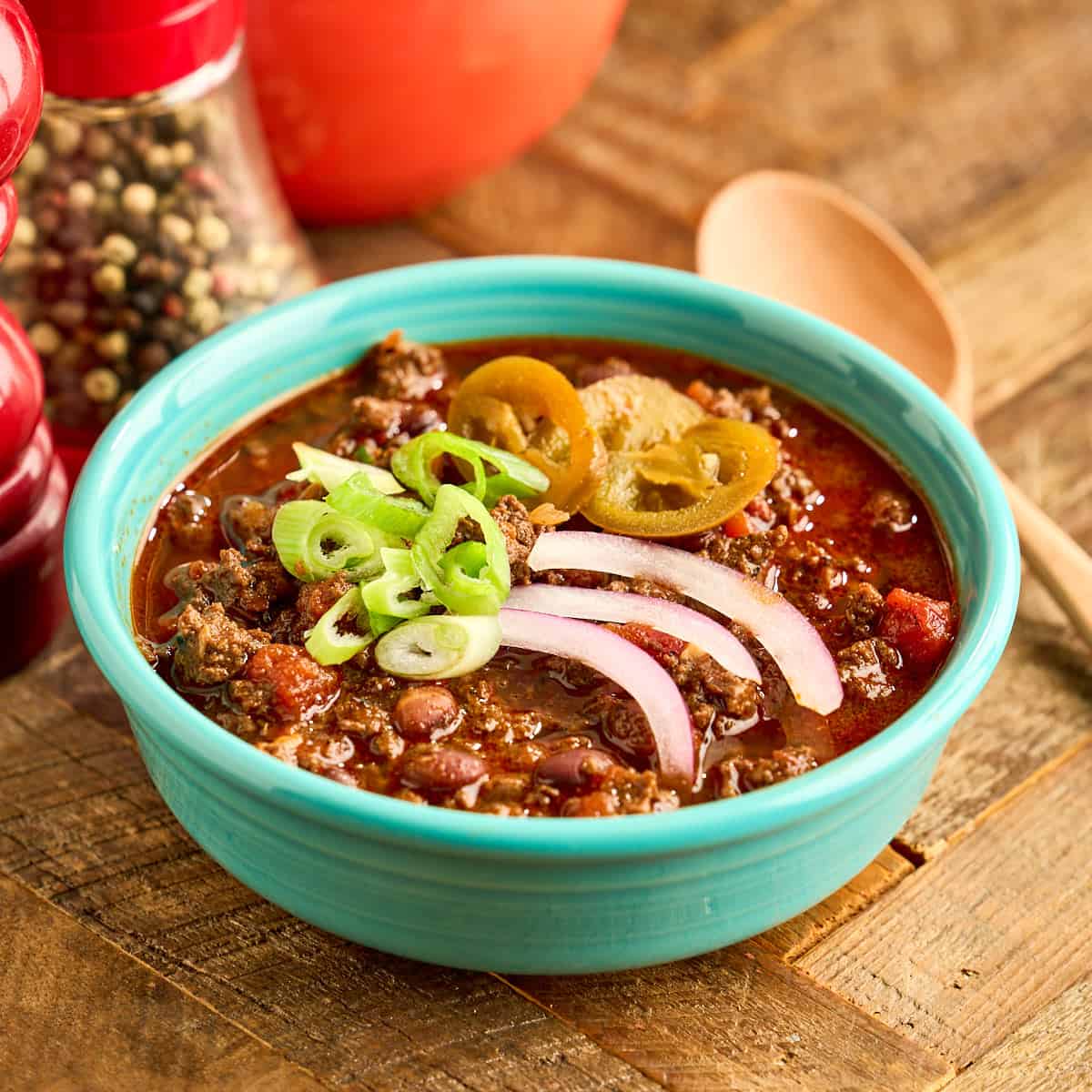 A bowl of Instant Pot Elk Chili topped with cheese, green onions, and pickled jalapenos